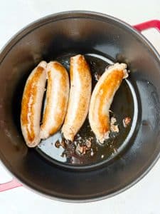 Browned sausages in a red Dutch oven for red cabbage with sausage recipe