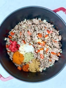 Lean ground beef cooking with onion, bell pepper, tomato paste, and spices like cumin, chili powder, and oregano in a Dutch oven.