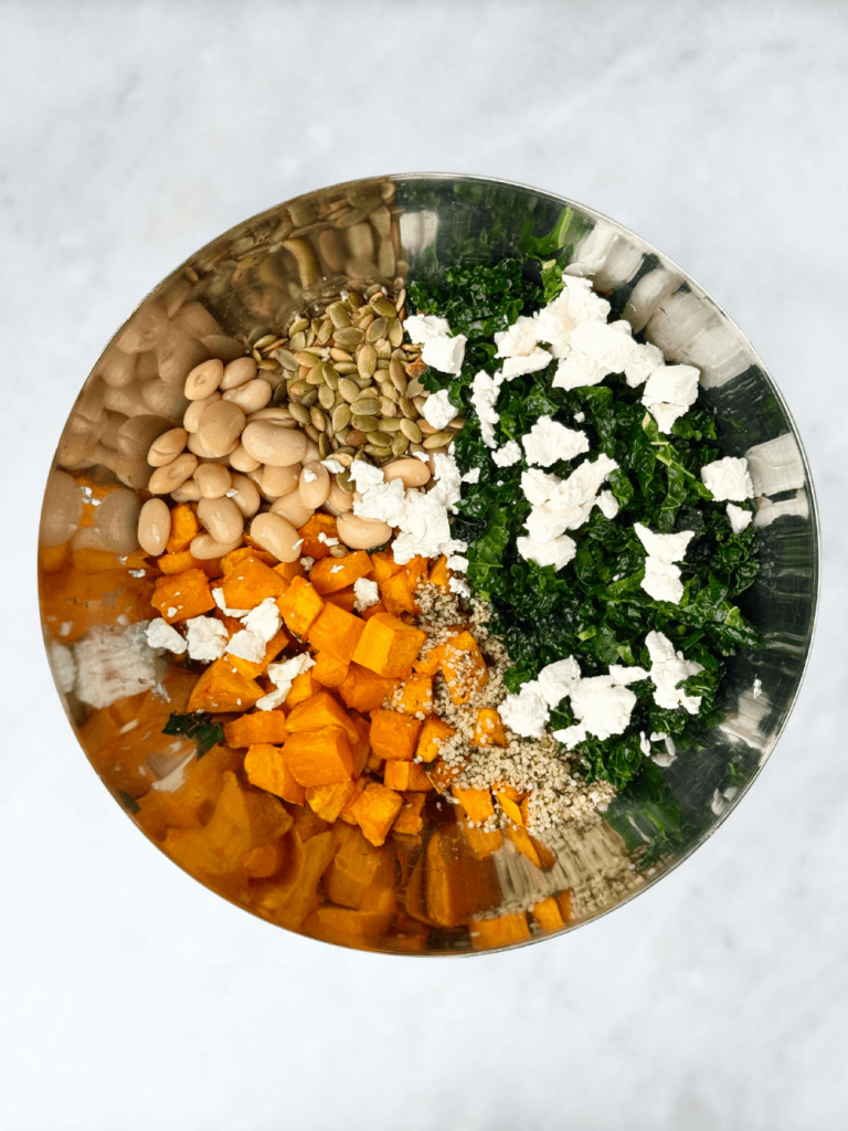 Overhead shot of salad ingredients—roasted pumpkin, kale, butter beans, hemp hearts, and goat cheese—before mixing.