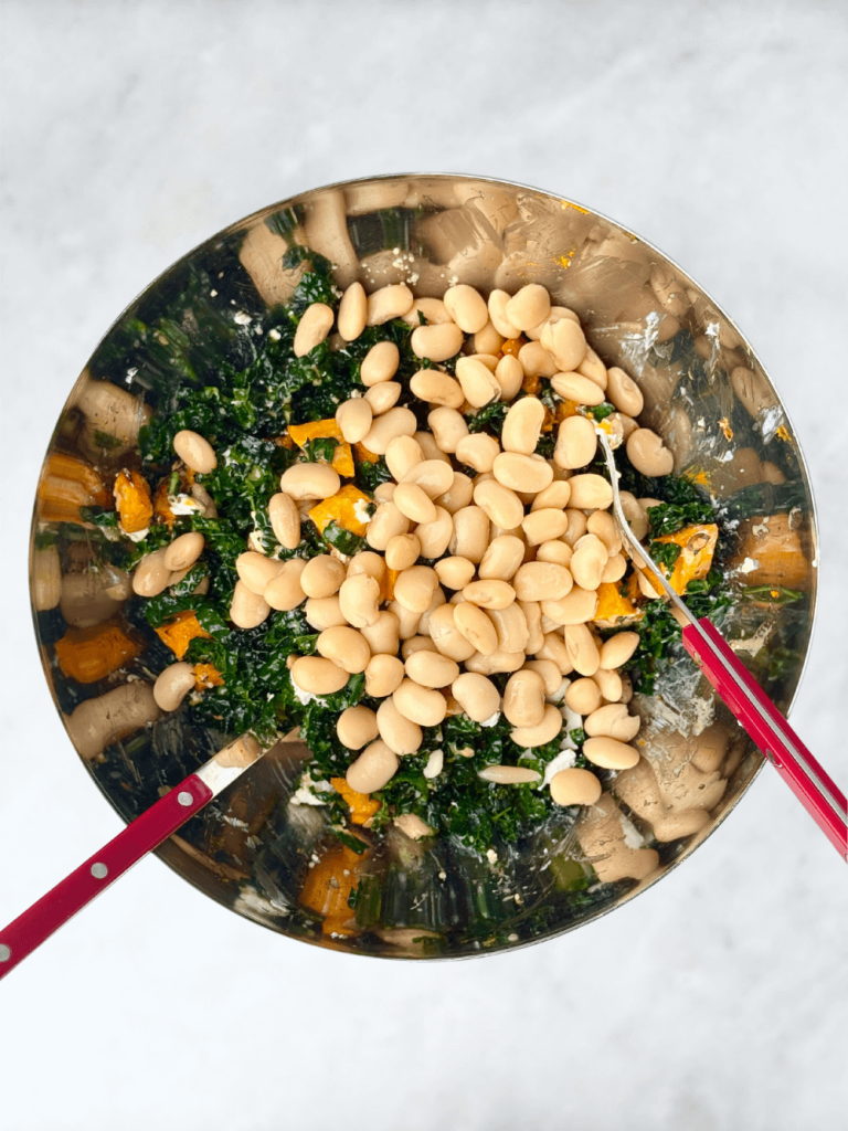 Butter beans added to kale and roasted pumpkin in a stainless steel bowl before tossing into salad.