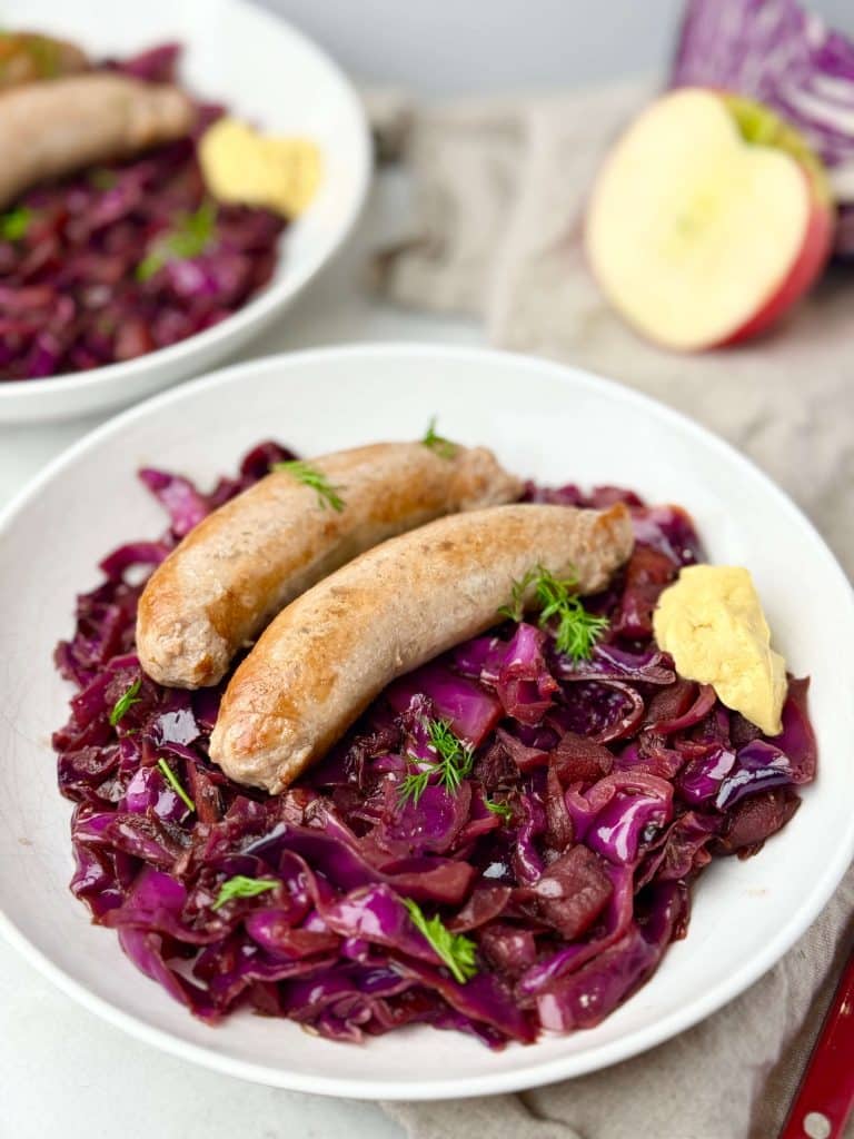 Tender sausages over braised red cabbage with apples and dill, ready to serve for a hearty dinner