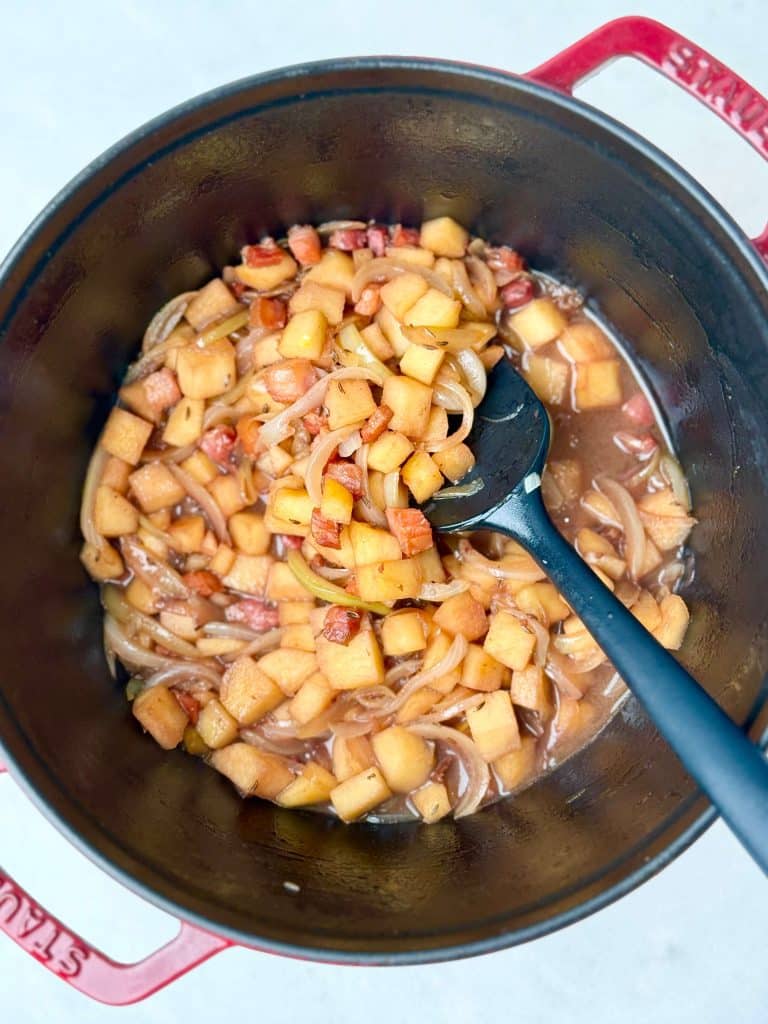 Sautéed apples, onions, and bacon in a Dutch oven for German red cabbage with sausage