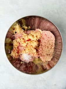 Mixing bowl filled with ground chicken, grated apple, salt, and spices for homemade breakfast sausages