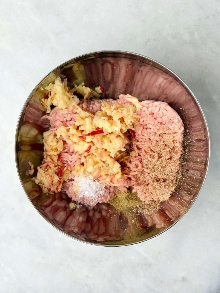Mixing bowl filled with ground chicken, grated apple, salt, and spices for homemade breakfast sausages