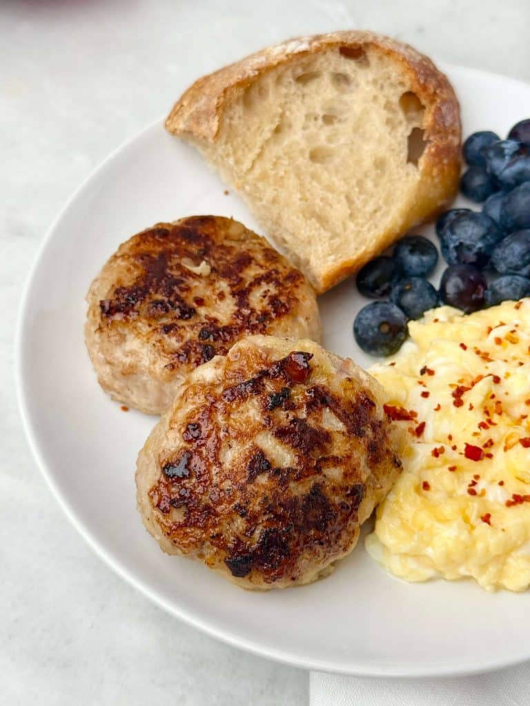Two homemade chicken apple sausage patties served with scrambled eggs, toast, and blueberries.