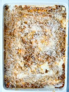 Homemade lasagna being assembled with layers of meat sauce, béchamel, and melted cheese.