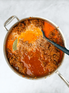 Bolognese sauce simmering in a pot with milk, chicken stock, and bay leaf for depth of flavor.