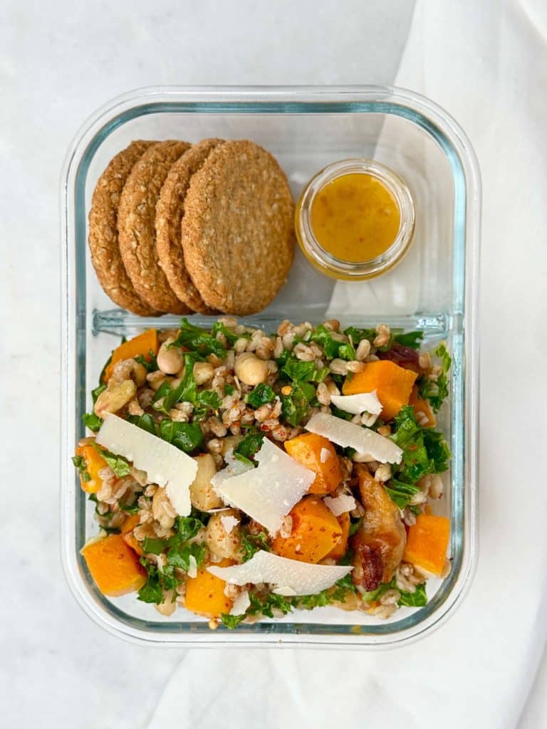 Meal prep container with fall farro salad, oat crackers, and honey lemon dressing for a cozy fall lunch.