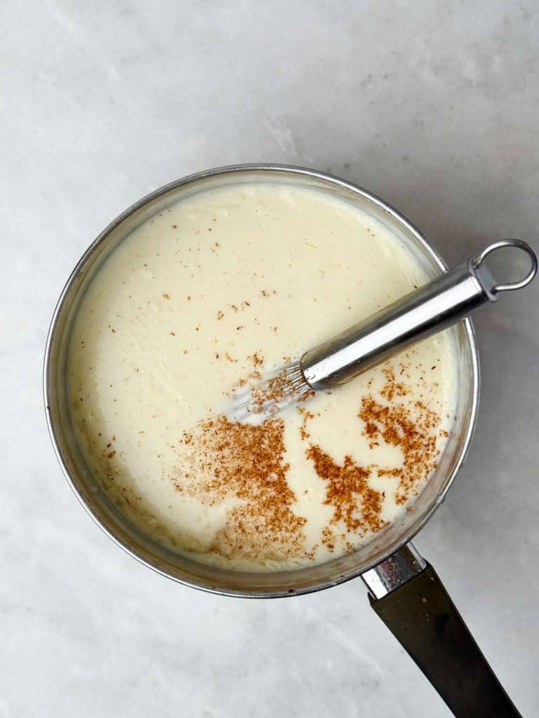 Creamy béchamel sauce in a saucepan with freshly grated nutmeg on top, ready for layering in lasagna.