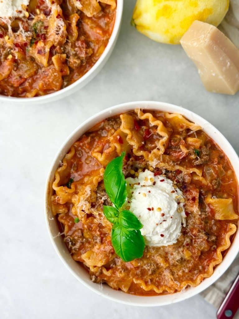 Bowl of creamy lasagna soup topped with ricotta, basil, and grated parmesan.