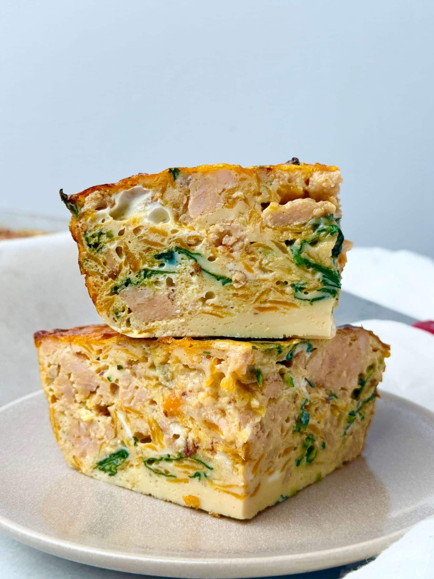 Two stacked slices of dairy-free breakfast casserole with sausage, sweet potato, and spinach on a neutral plate.