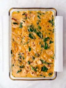 Unbaked breakfast casserole with sausage, spinach, and sweet potato mixture poured into a parchment-lined dish.