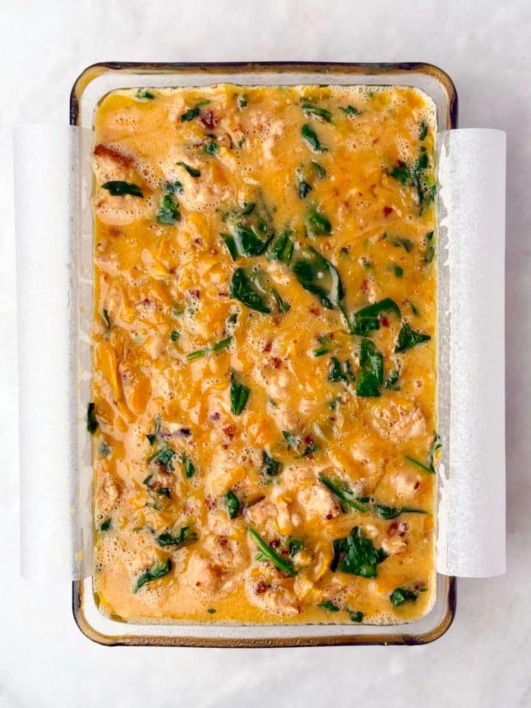 Unbaked breakfast casserole with sausage, spinach, and sweet potato mixture poured into a parchment-lined dish.