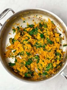 Sautéed shredded sweet potatoes and spinach in a skillet for the base of a dairy-free breakfast casserole.