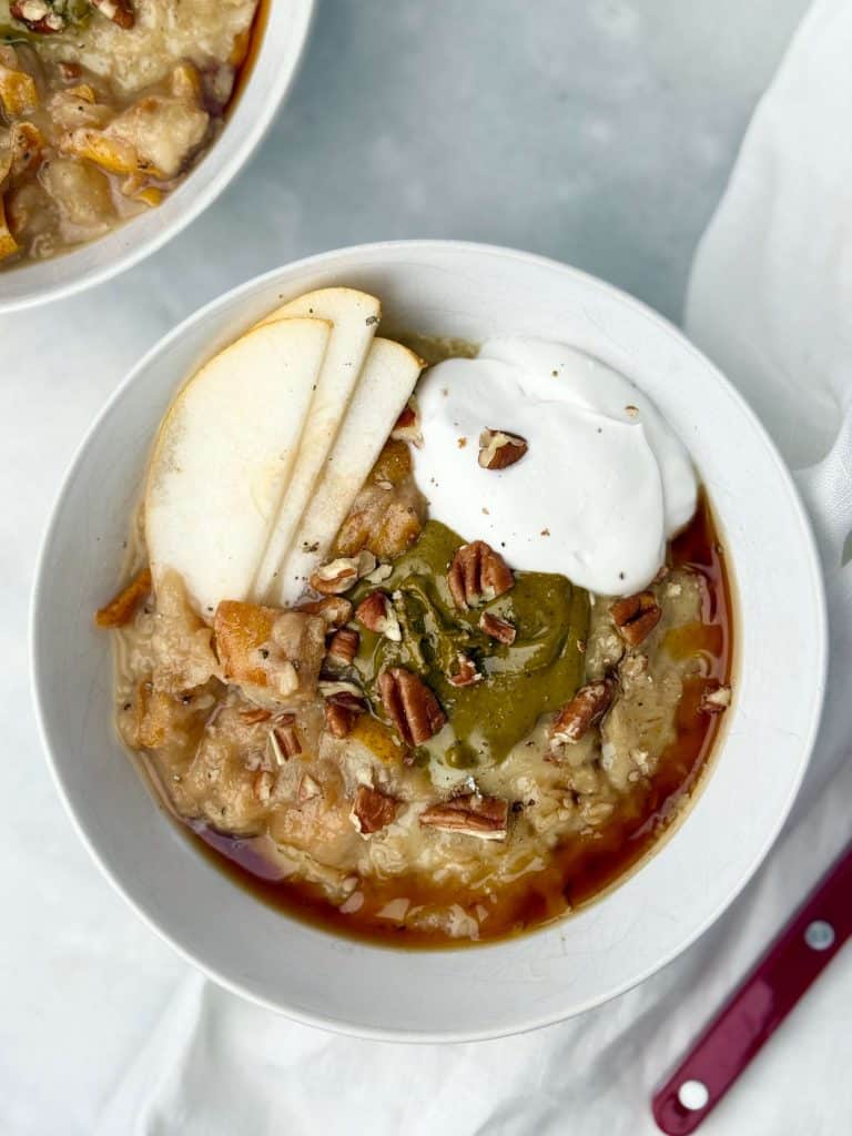 Overhead view of dairy-free protein oatmeal with creamy toppings of pear, pistachio butter, pecans, and coconut yogurt for a cozy breakfast.
