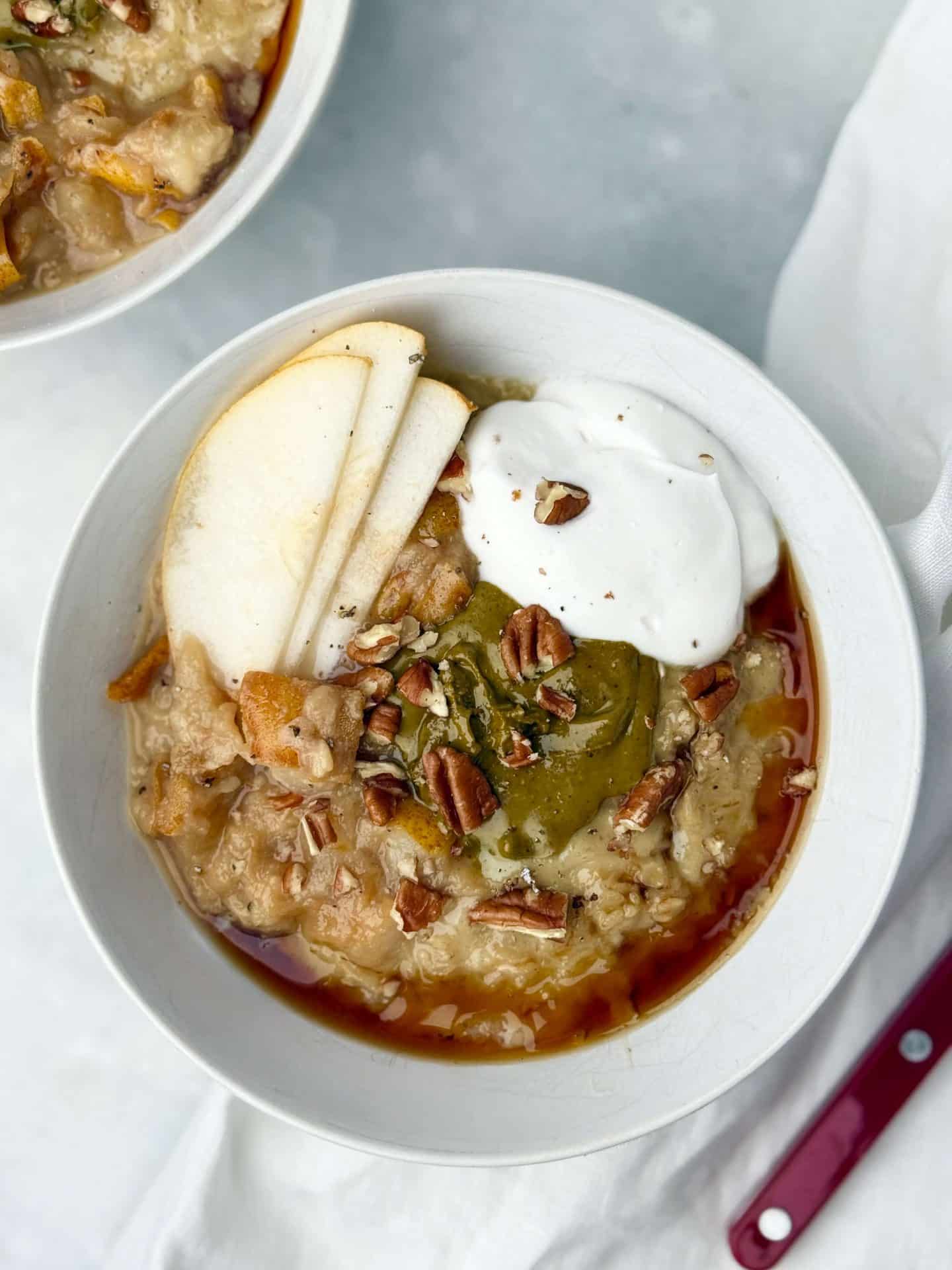 Overhead view of dairy-free protein oatmeal with creamy toppings of pear, pistachio butter, pecans, and coconut yogurt for a cozy breakfast.