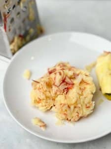 Freshly grated apple on a plate with a box grater, ready to be mixed into chicken breakfast patties