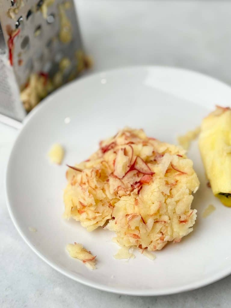 Freshly grated apple on a plate with a box grater, ready to be mixed into chicken breakfast patties