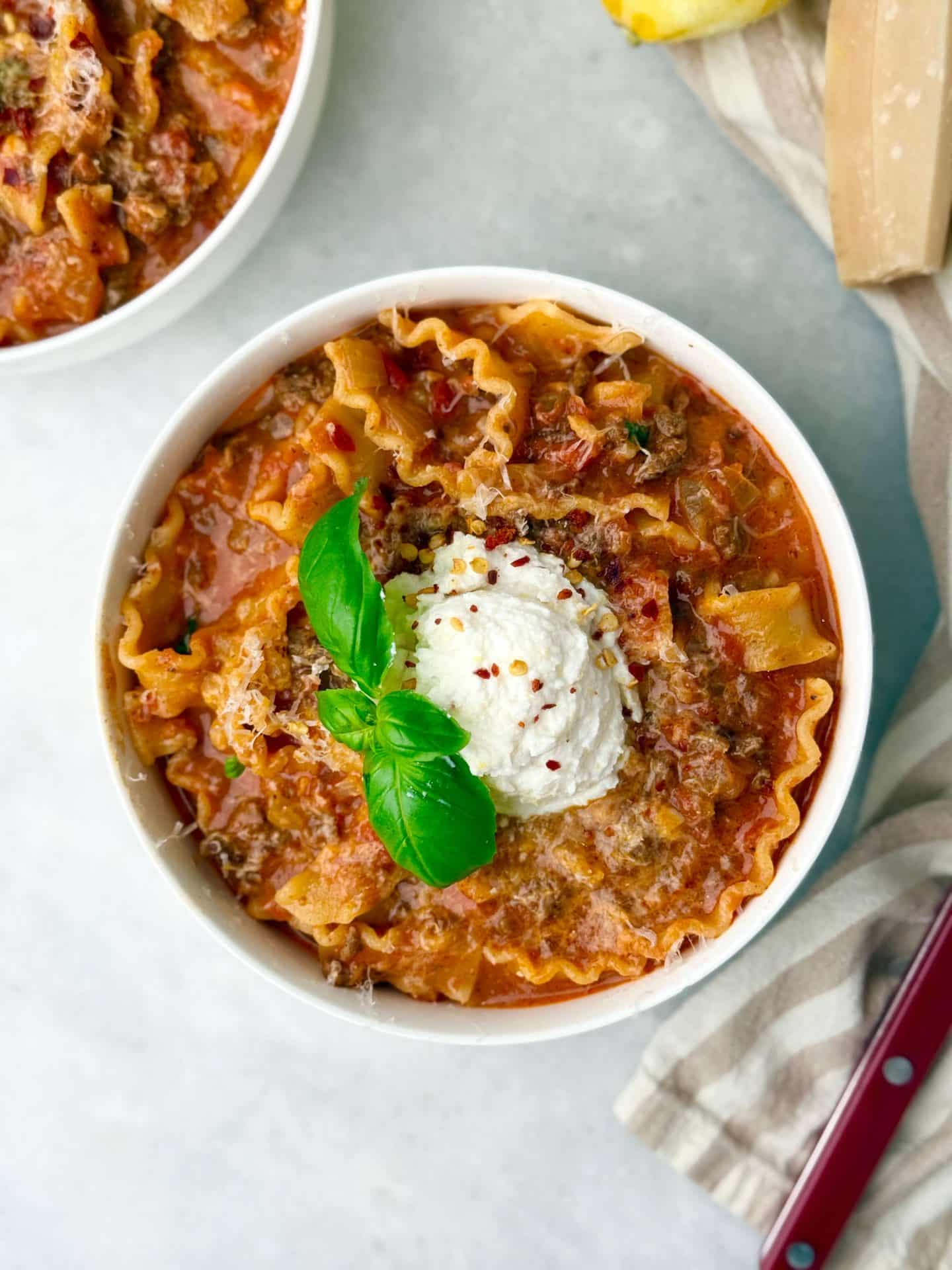 Bowl of creamy high-protein lasagna soup topped with lemon ricotta, basil, and red pepper flakes.