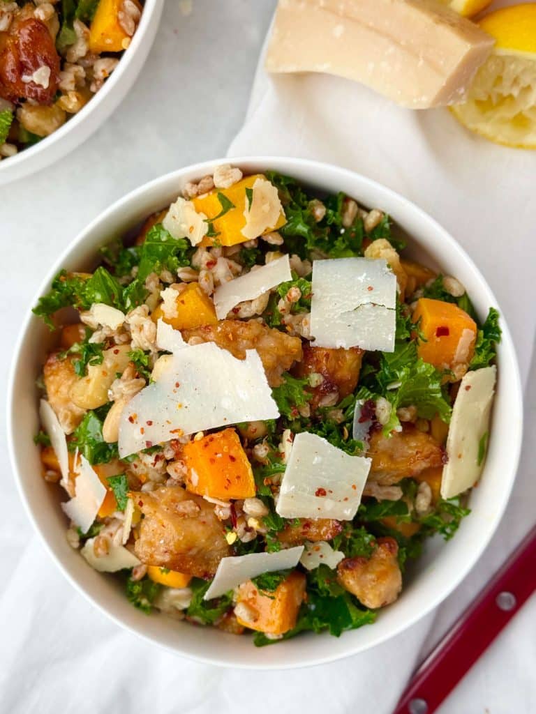 Bowl of fall farro salad with butternut squash, kale, white beans, sausage, and shaved parmesan.