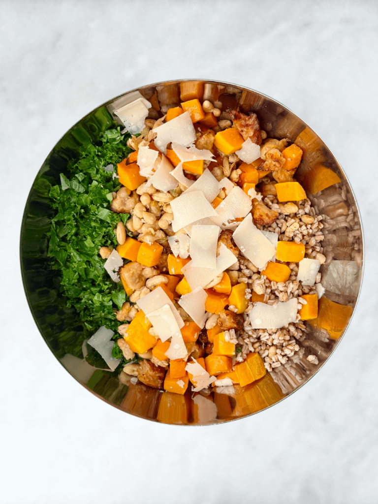 Mixing bowl filled with farro, butternut squash, white beans, kale, and parmesan shavings for a fall grain bowl.
