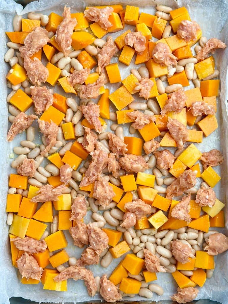 Roasting tray with cubed butternut squash, white beans, and sausage pieces before baking for a fall farro salad.