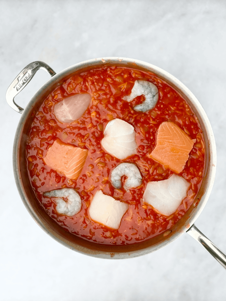 Pieces of cod, salmon, and shrimp nestled into a simmering spicy tomato sauce before poaching.