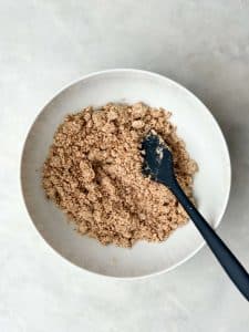 Protein cinnamon crumble mixture in a white bowl with a spatula for topping apple muffins.