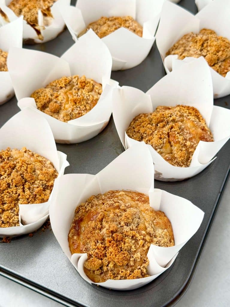 Tray of freshly baked Greek yogurt apple cinnamon muffins in white parchment liners with golden crumble topping.