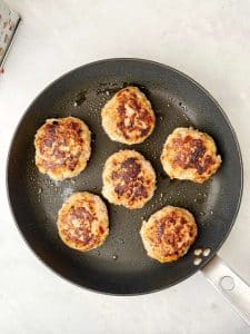 Chicken apple sausage patties sizzling in a skillet with a crisp golden brown crust
