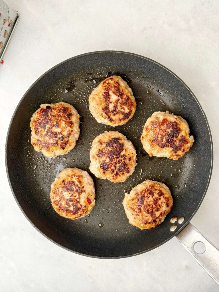 Chicken apple sausage patties sizzling in a skillet with a crisp golden brown crust