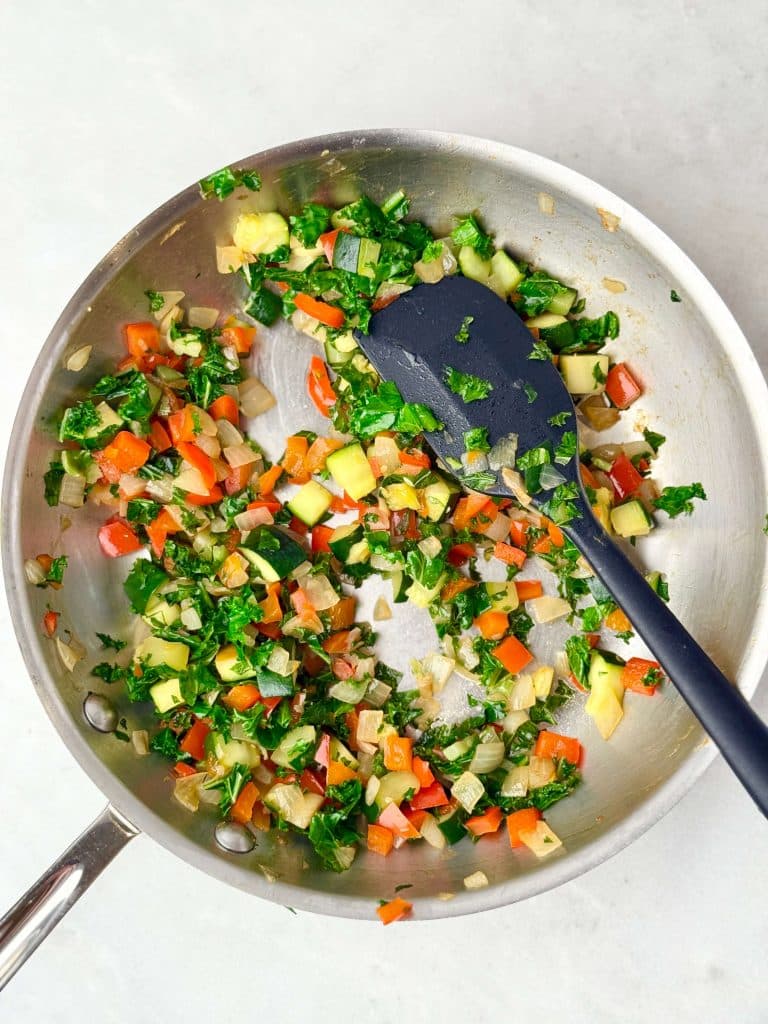 Sautéed kale, zucchini, bell pepper, and onion mixture in skillet for high-protein dairy-free frittata cups