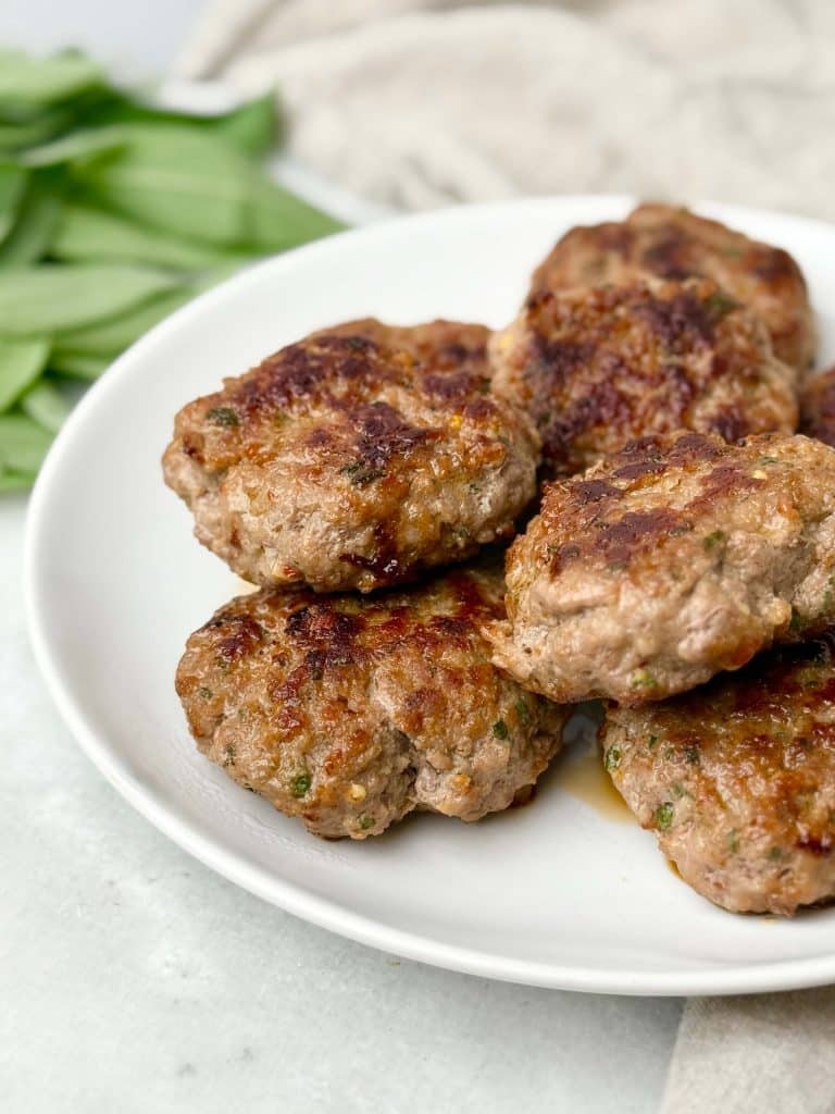 Healthy maple sage turkey sausage patties stacked on a white plate for a protein-packed breakfast.