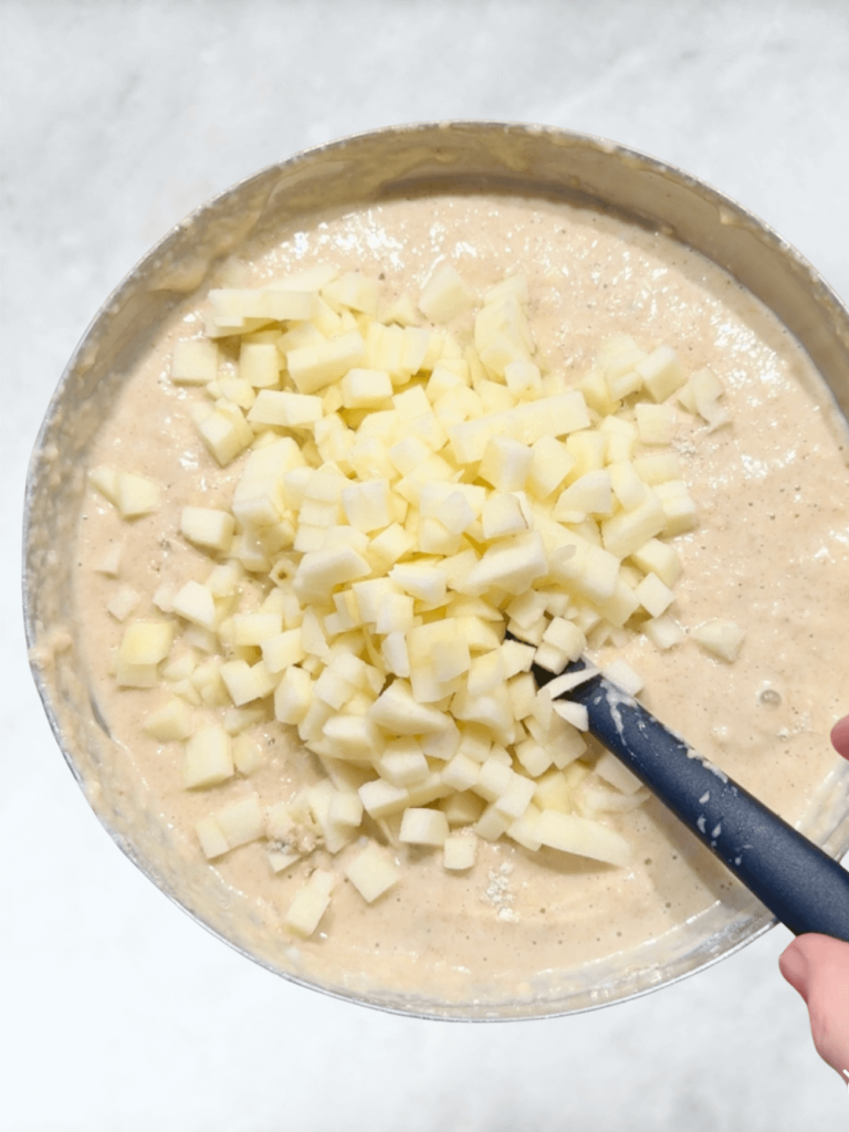 Diced fresh apples being folded into muffin batter for healthy high-protein apple cinnamon muffins.