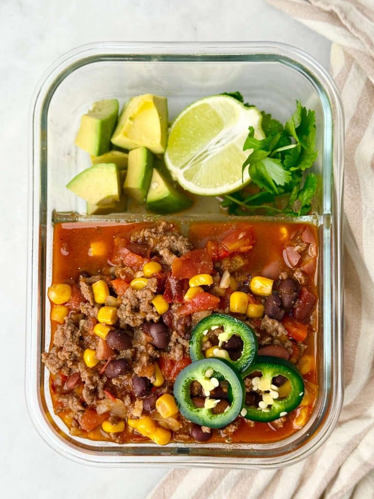 Meal prep container filled with high-protein beef taco soup, avocado, lime, and cilantro for an easy under-500-calorie lunch.