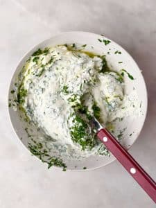 Bowl of creamy Greek yogurt sauce with parsley, tarragon, and dill for serving with roasted spatchcock chicken.