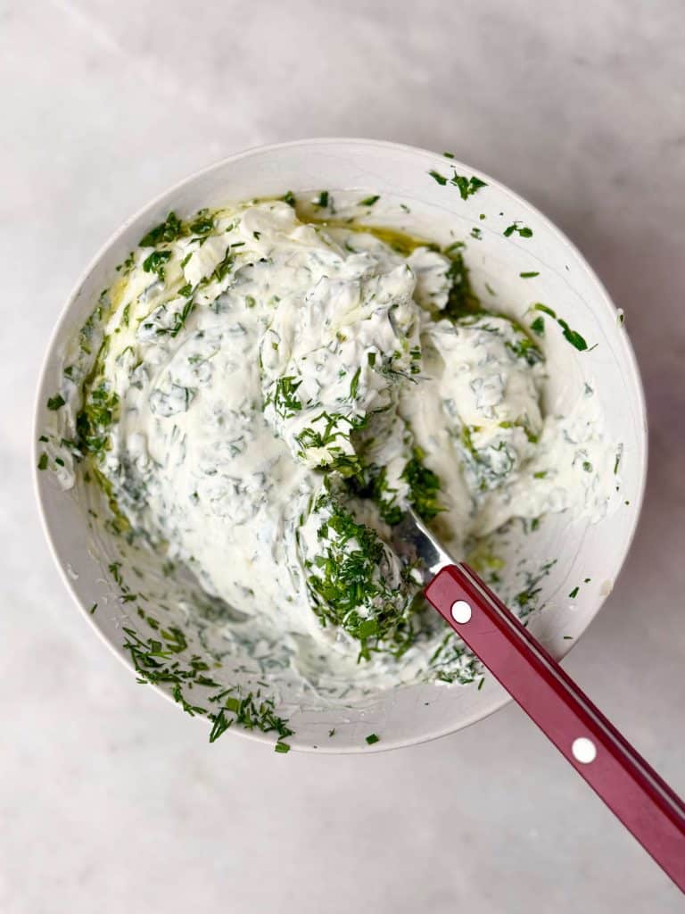 Bowl of creamy Greek yogurt sauce with parsley, tarragon, and dill for serving with roasted spatchcock chicken.
