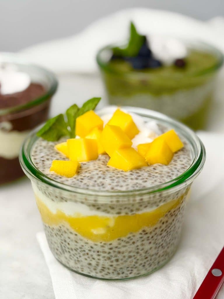 Coconut mango dairy free chia seed pudding layered with mango purée and coconut cream, topped with fresh mango cubes and mint in a glass jar.
