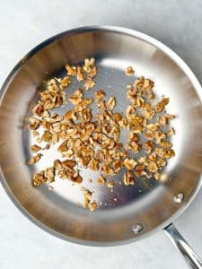 Chopped walnuts being toasted in a stainless steel skillet for apple walnut chicken salad recipe.