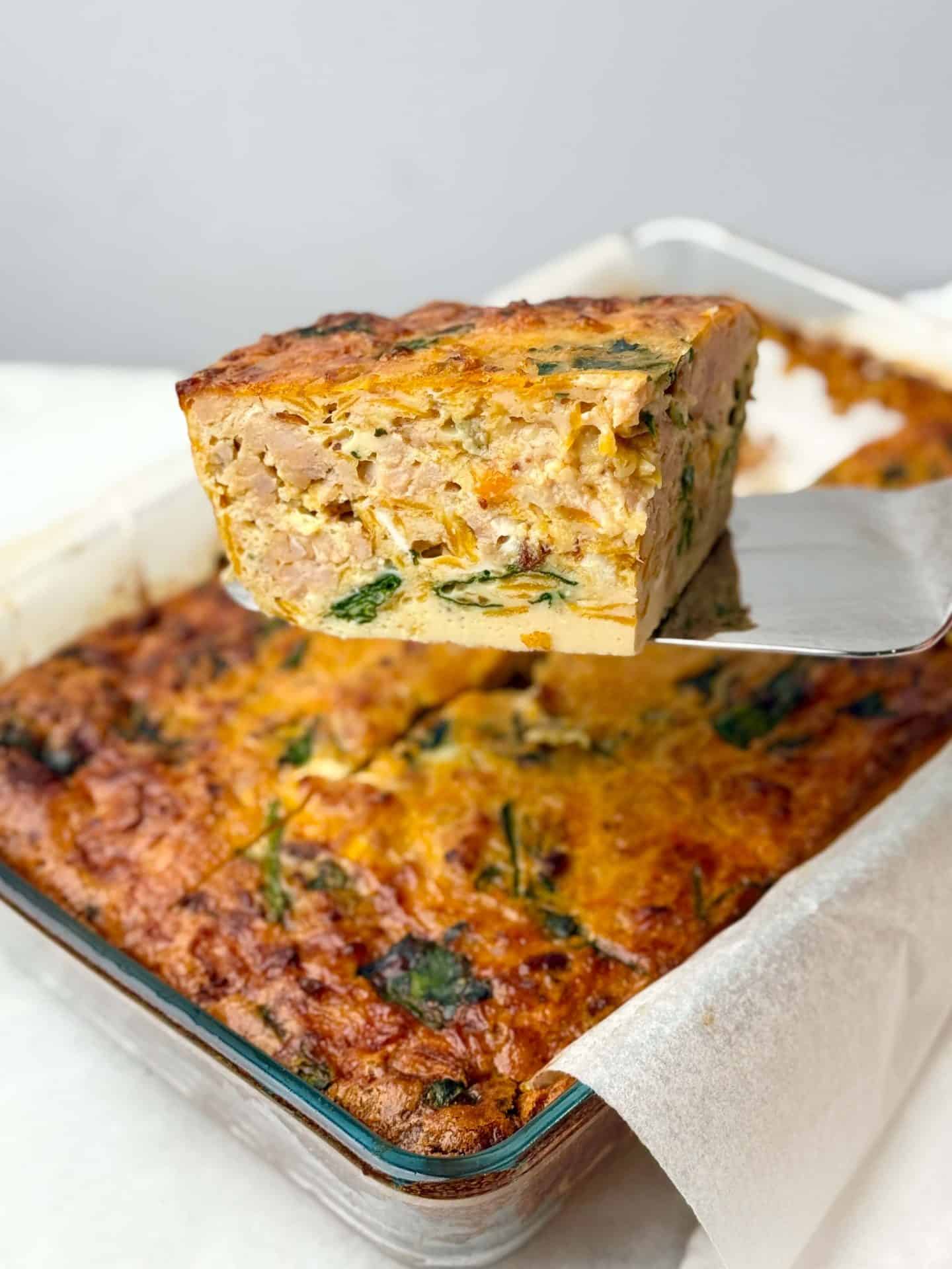 Slice of dairy-free breakfast casserole lifted from a baking dish with sausage and spinach visible.