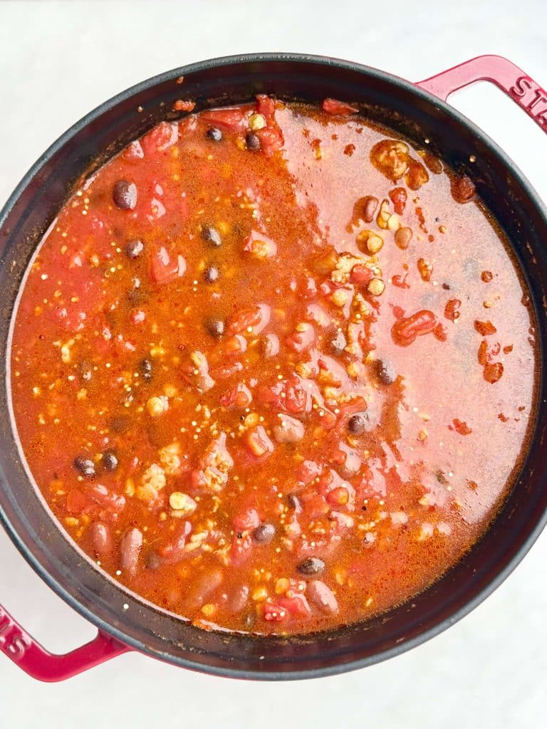 Simmering high protein low calorie turkey chili with beans, lentils, and quinoa in a red Dutch oven.