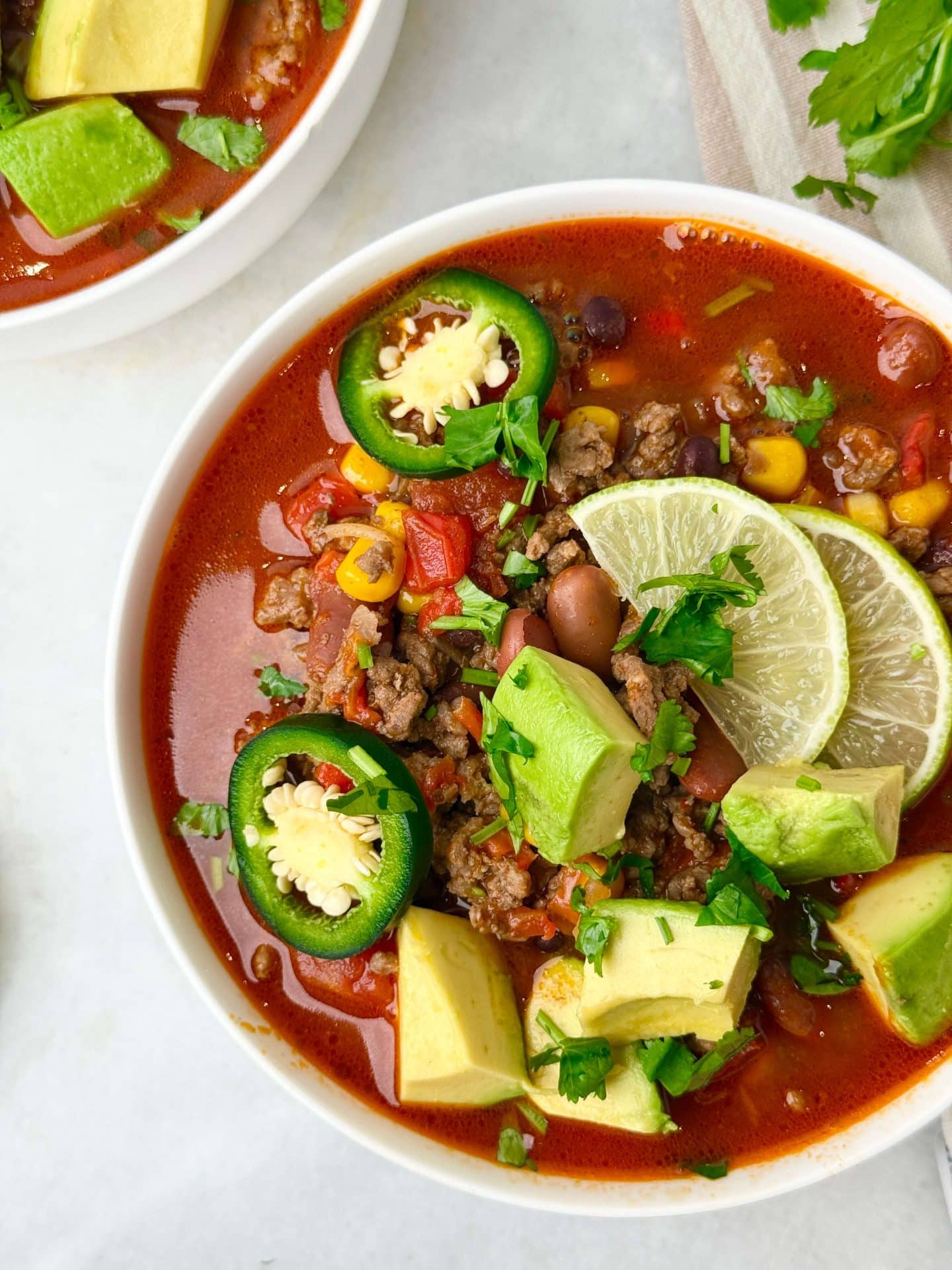 Close-up of high-protein beef taco soup with lean ground beef, avocado chunks, lime slices, and fresh cilantro.