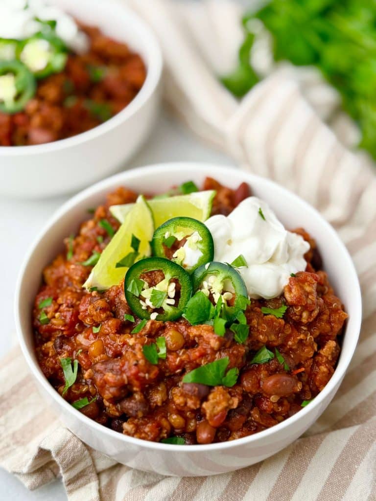 Bowl of turkey chili with lentils and quinoa topped with avocado, sour cream, jalapeño slices, and lime.