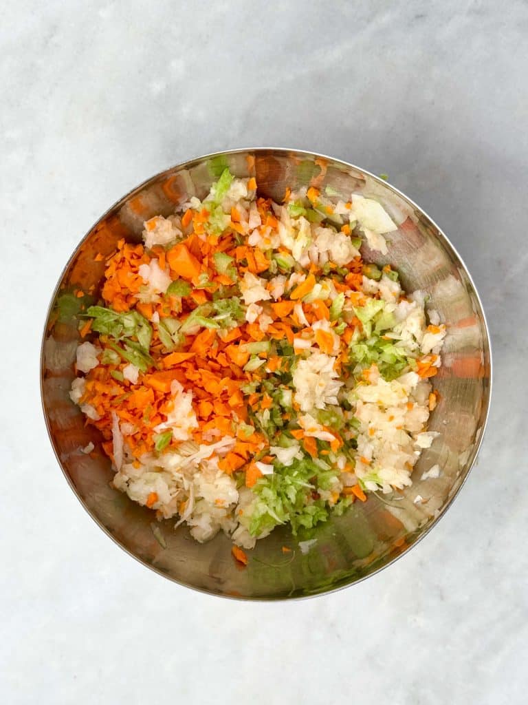 Finely chopped onion, celery, carrot, and garlic in a mixing bowl for homemade bolognese sauce.