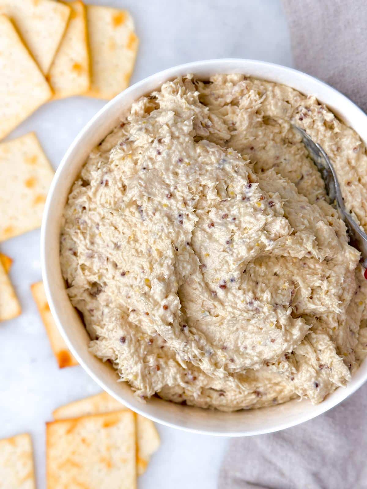 Creamy honey mustard chicken salad in a white bowl with a spoon and pita crackers