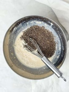 Chia seeds being whisked into a bowl of dairy free milk and protein mixture to make chia pudding.