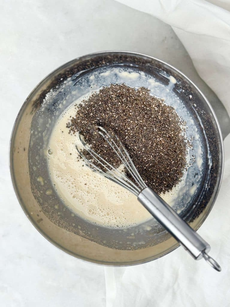 Chia seeds being whisked into a bowl of dairy free milk and protein mixture to make chia pudding.