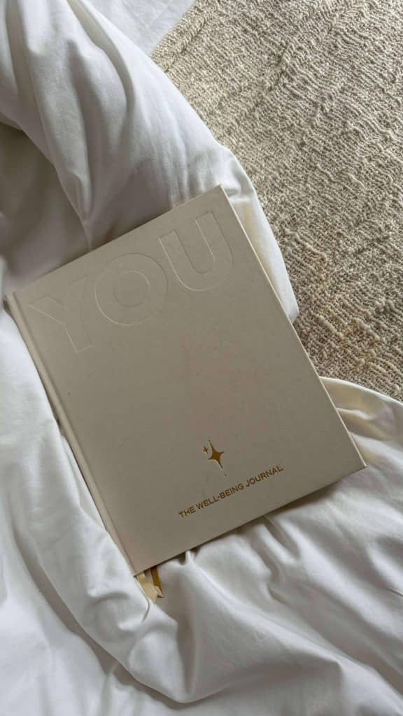 Soft beige wellness journal resting on white bedding, symbolizing reflection and mindfulness for vision boarding.