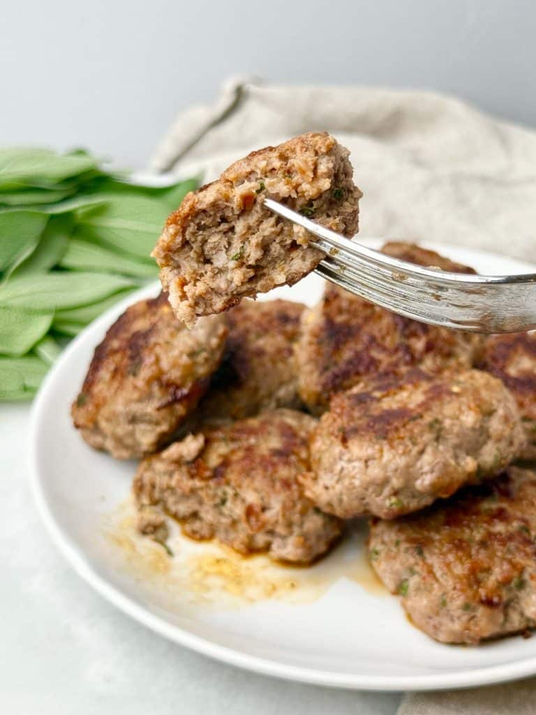 Close-up of a juicy maple sage turkey sausage patty on a fork showing tender texture and herbs.