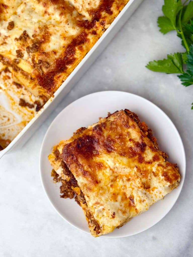 A square of baked lasagna with rich meat sauce and creamy béchamel served on a plate, fresh parsley on the side.